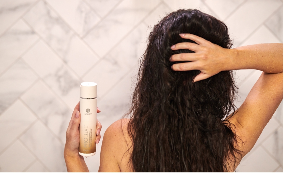 Image of woman's hair while she holds a bottle of ProLuxe Shampoo.